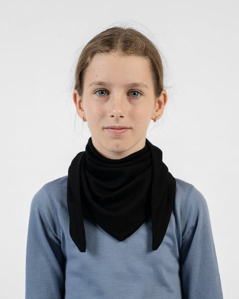 A young girl wearing a black merino bandana tied around her neck with the triangular point resting on her chest.