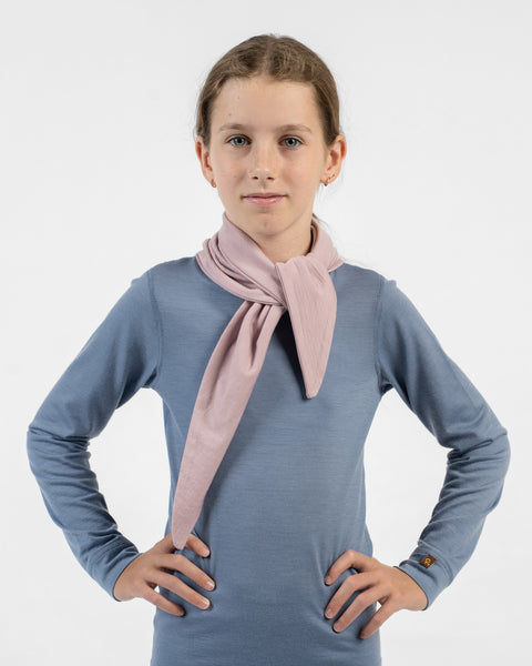 A young girl with her hands on her hips, wearing a dusty pink merino bandana tied around her neck like a scarf with the ends hanging loosely down the front.