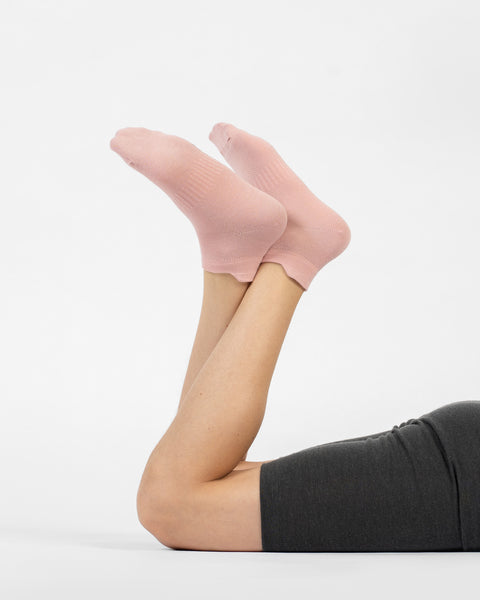 A person lying on their stomach with their lower legs raised, modeling a pair of dusty pink cotton ankle socks.