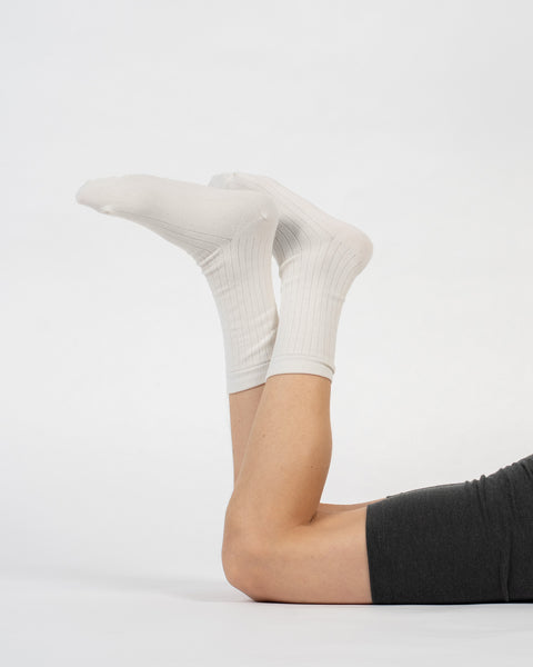 A person lying on their stomach with their lower legs raised, modeling natural ribbed merino crew socks.