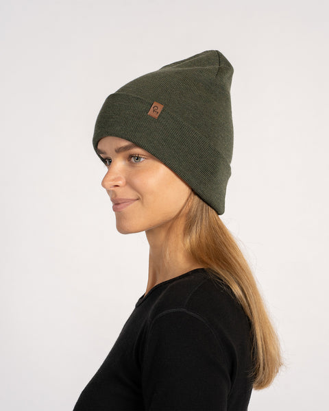 Woman in a dark green knitted merino wool beanie, turned sideways to the left, showing the profile of the hat.