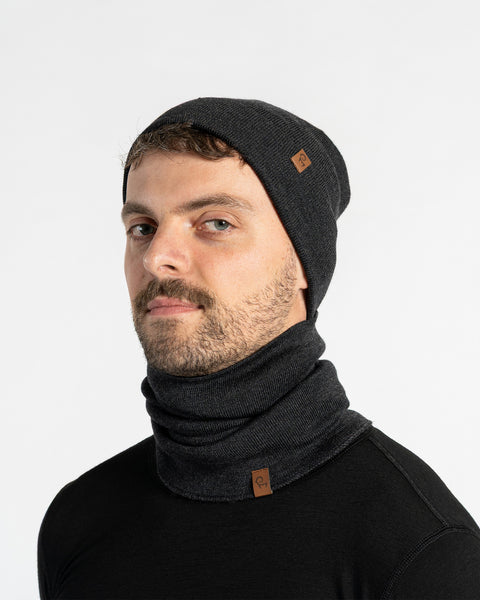 Man wearing a dark gray knit beanie and scarf on a light gray background