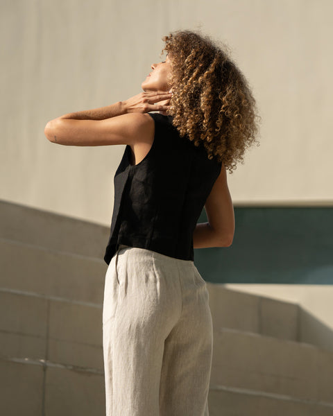 Linen vest ava in black paired with natural color linen pants. Women is sitting and smiling