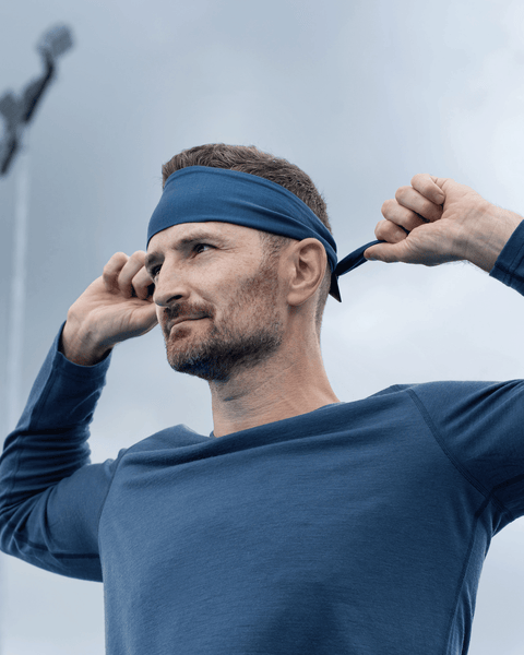 A man wearing a dark blue long-sleeved athletic shirt adjusting a blue headband around his head outdoors.