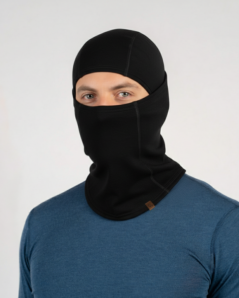 Close-up of a man in a blue top wearing a black Merino wool balaclava, photographed against a plain background.