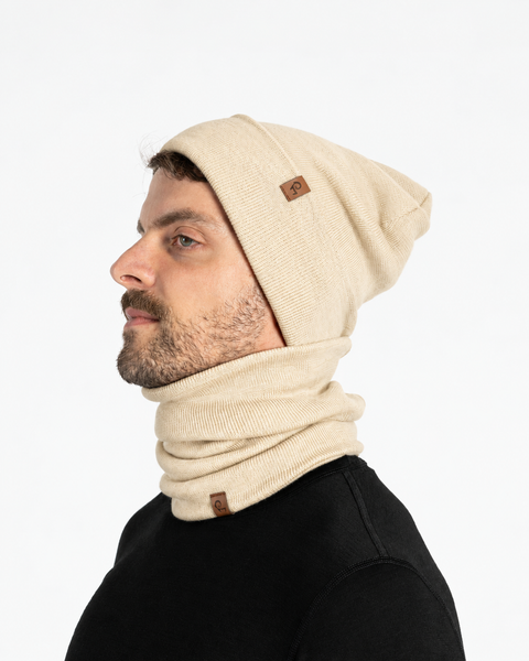 Profile view of a man in a black shirt wearing a beige beanie and a matching beige neck gaiter around his neck.