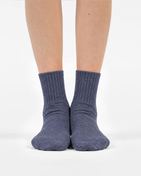 A front-facing view of a person's lower legs and feet standing side-by-side in heathered blue crew socks.