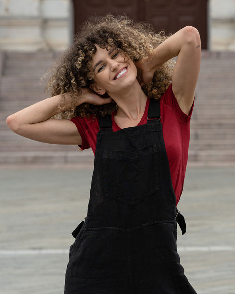Beautiful woman with curly hair posing in the city wearing pure black linen jumpsuit Nicci, royal cherry merino wool top.