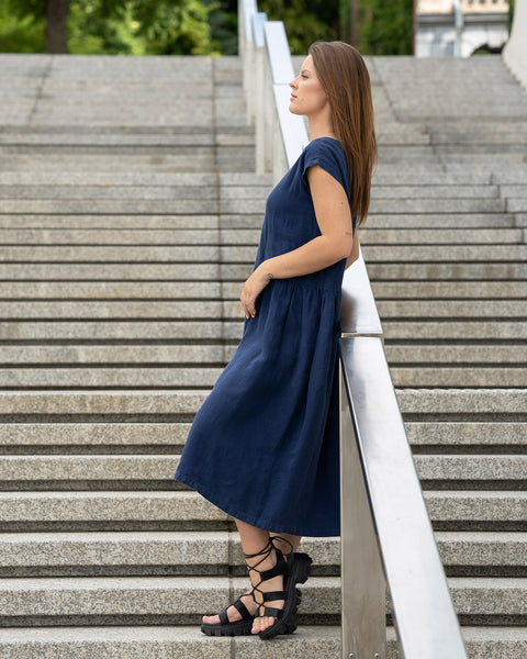Young woman posing in a city street on stears wearing linen smock dress cecilia in a storm blue color.