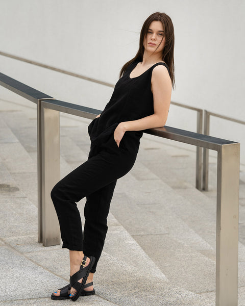 A young girl posing outdoors in a city on a concrete stairs, wearing linen pure black tank top Hana, and pure black pants dakota.