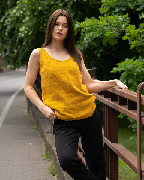 A young woman posing in a city street wearing linen set with a spicy yellow tank top Hana and pure black linen pants Dakota.