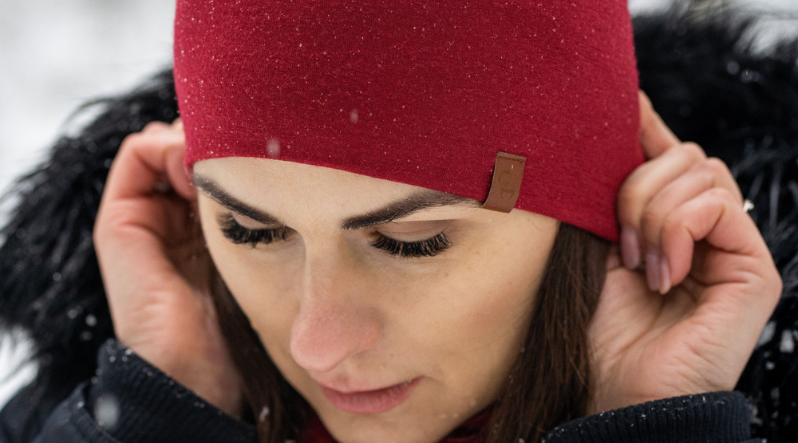 A woman wearing a royal cherry merino wool beanie while it is snowing outside.