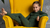 a girl sitting in a bright yellow ottoman, wearing a mat ching set of the merino wool kids' clothing: a long sleeve shirt and pants in dark green color.