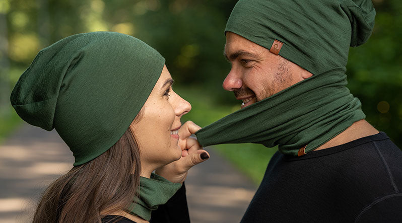 In the photo you can see couple's faces, they are staring at each other. Woman and man are wearing matching dark green neck gaiters and slouchy beanies, made from natural and warm 100% Merino wool.