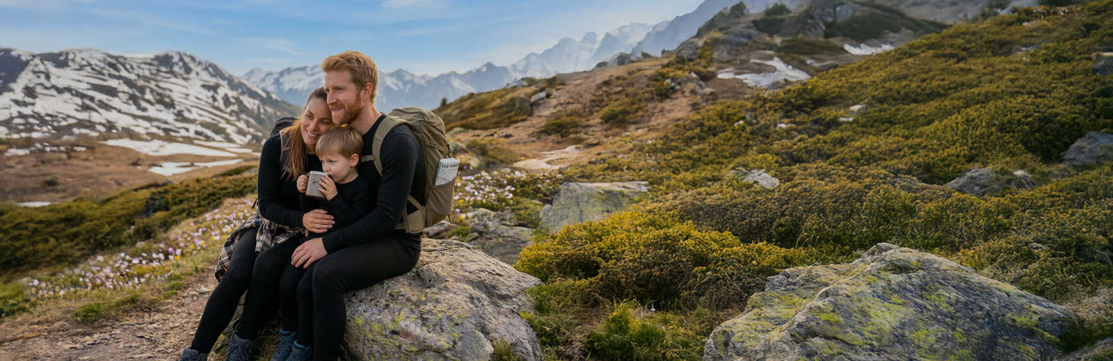 Family resting during mountain hike wearing merino wool base layers, breathable temperature-regulating clothing for outdoor adventures and trekking in the mountains.