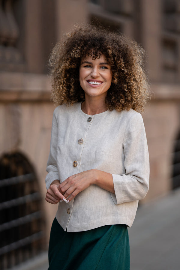 A model wearing a natural beige linen jacket Alice with buttons, featuring a relaxed fit, 3/4-length sleeves, and a minimalist design. The jacket is paired with matching dark green skirt