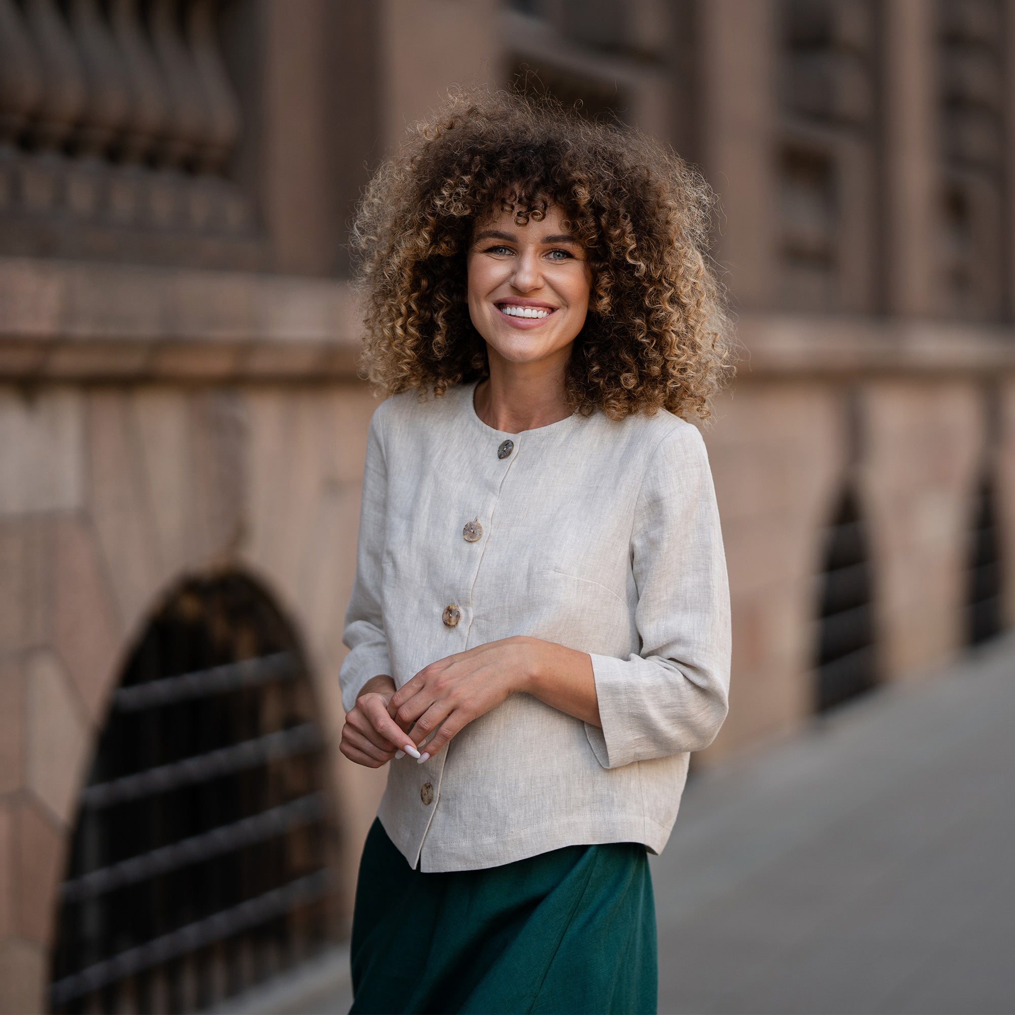 A model wearing a natural beige linen jacket Alice with buttons, featuring a relaxed fit, 3/4-length sleeves, and a minimalist design. The jacket is paired with matching dark green skirt