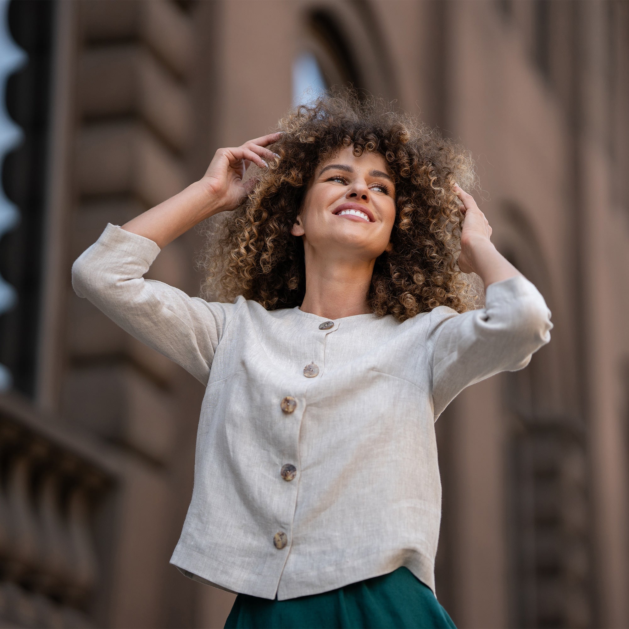 Woman with curly hair wearing almond brown linen jacket Alice and standing in  astreet