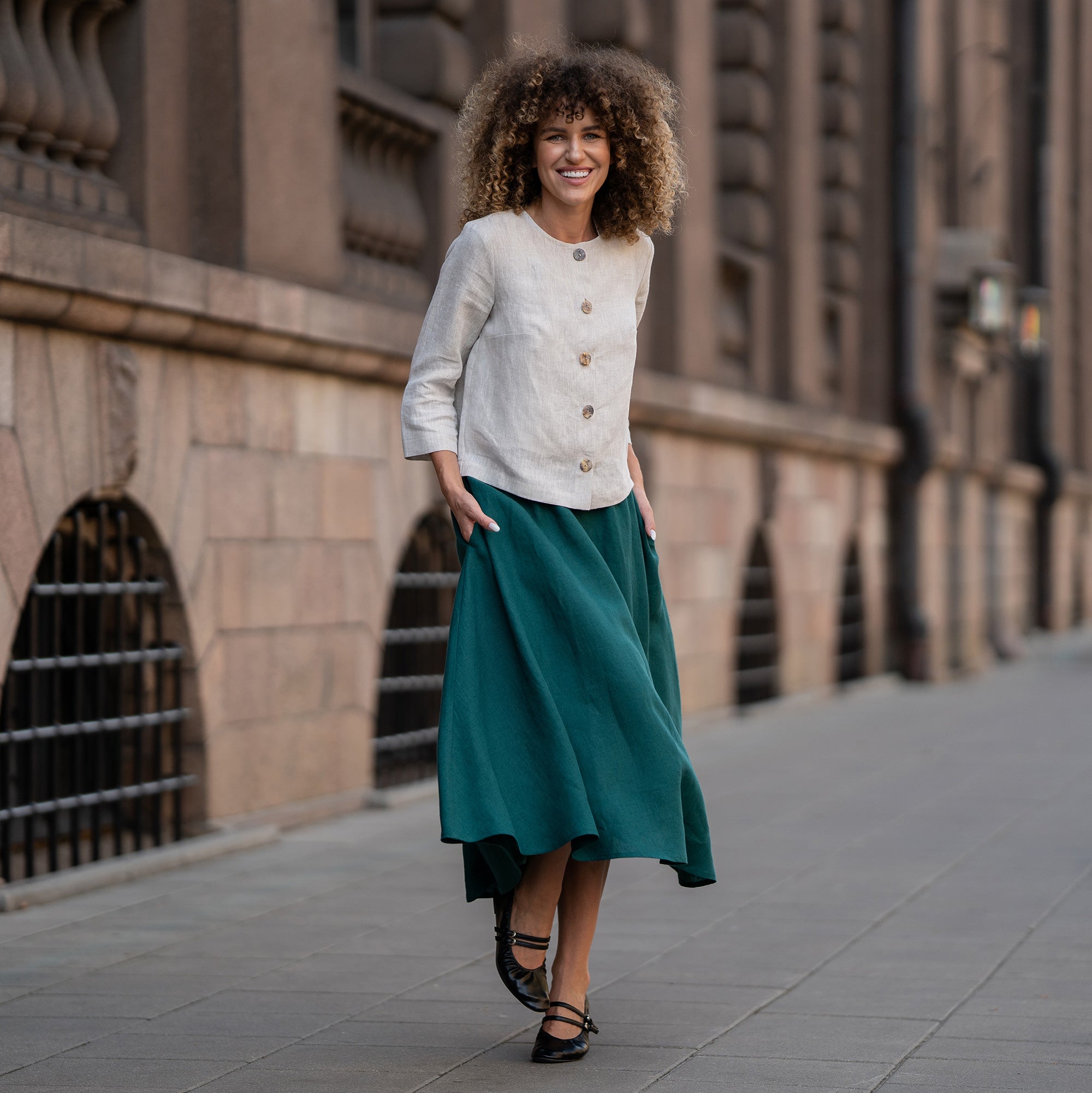 A model wearing a natural beige linen jacket Alice with buttons, featuring a relaxed fit, 3/4-length sleeves, and a minimalist design. The jacket is paired with matching dark green skirt