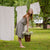 In this picture the model is standing in front of a clothesline with white garments hanging on it. Beside her is a metal bucket full of flowers. She is visible full-height, as well as the full skirt length. The skirt is knee length, matched with a same pattern blouse.