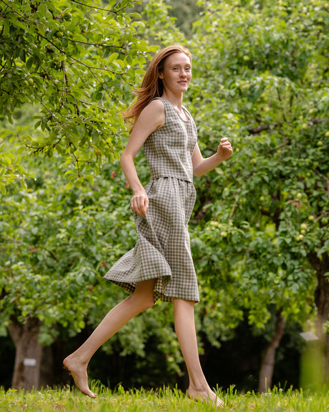 In this photograph the model is wearing the matching crop top and skirt set in green gingham. She is captured during a movement, while she is running - her hands and feet are in a relaxed position and she is slightly above the ground.  The picture highlights the length of the garments.
