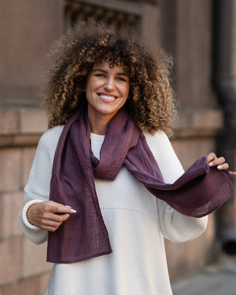 Elegant plum-colored European washed linen scarf draped over white knit sweater showing lightweight fabric texture by Menique