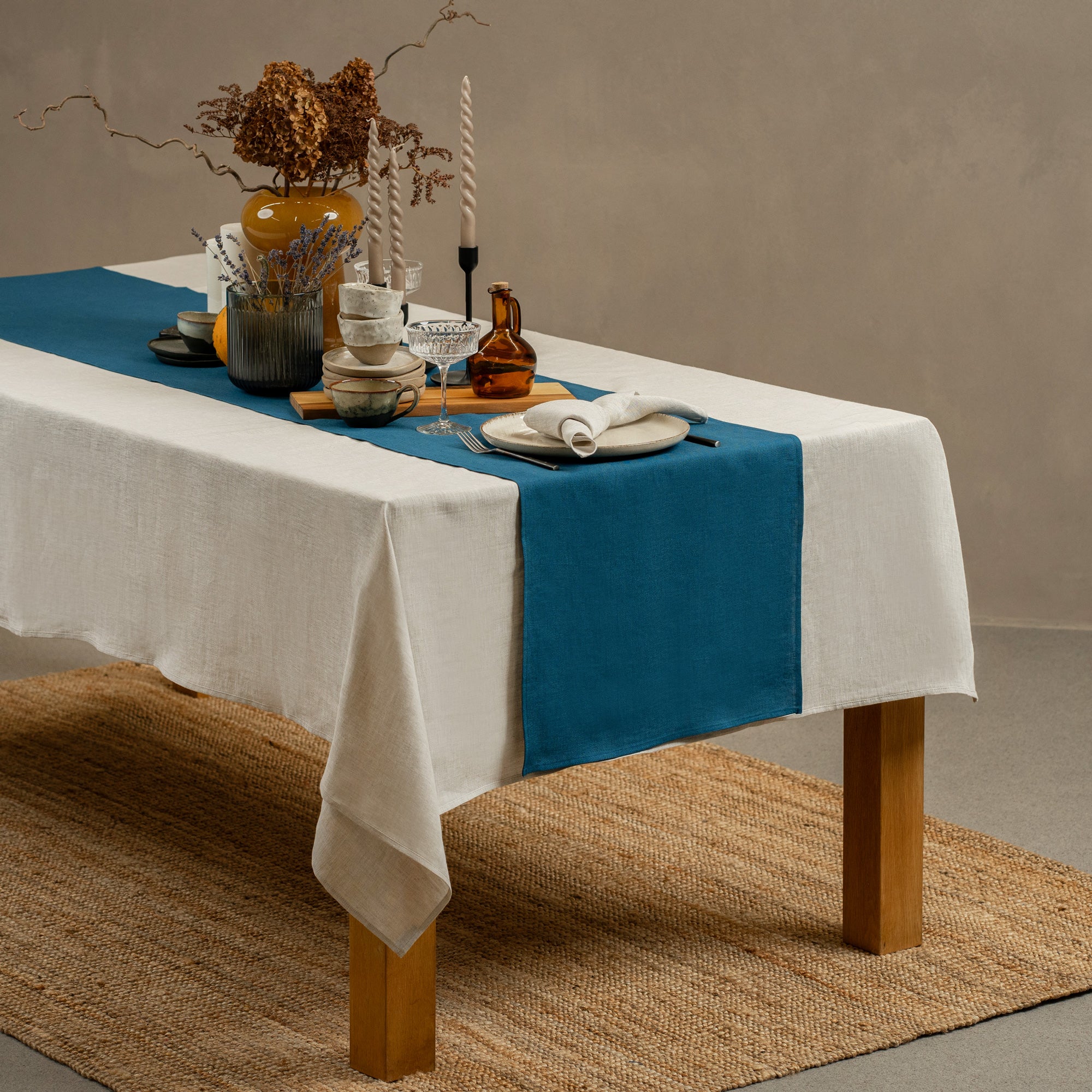 A wooden table positioned on top of a carpet. There is a dark green linen table runner and a vase on top.