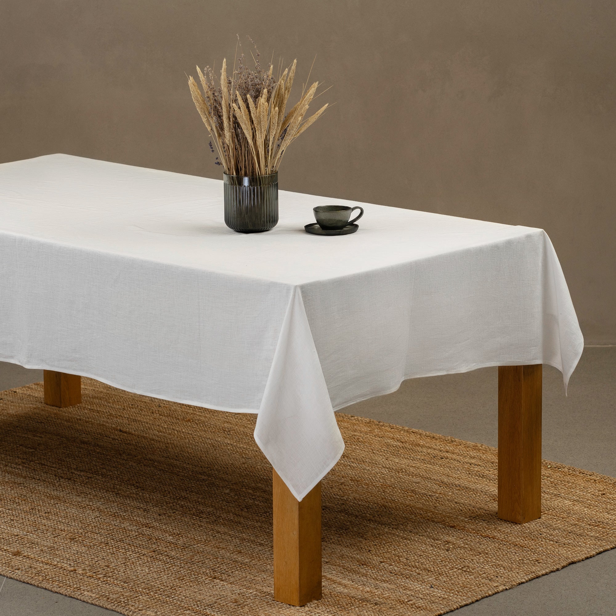 The menique linen tablecloth in spicy yellow color, draping over a wooden table, with a vase, wooden board and a glass bottle on top of it.