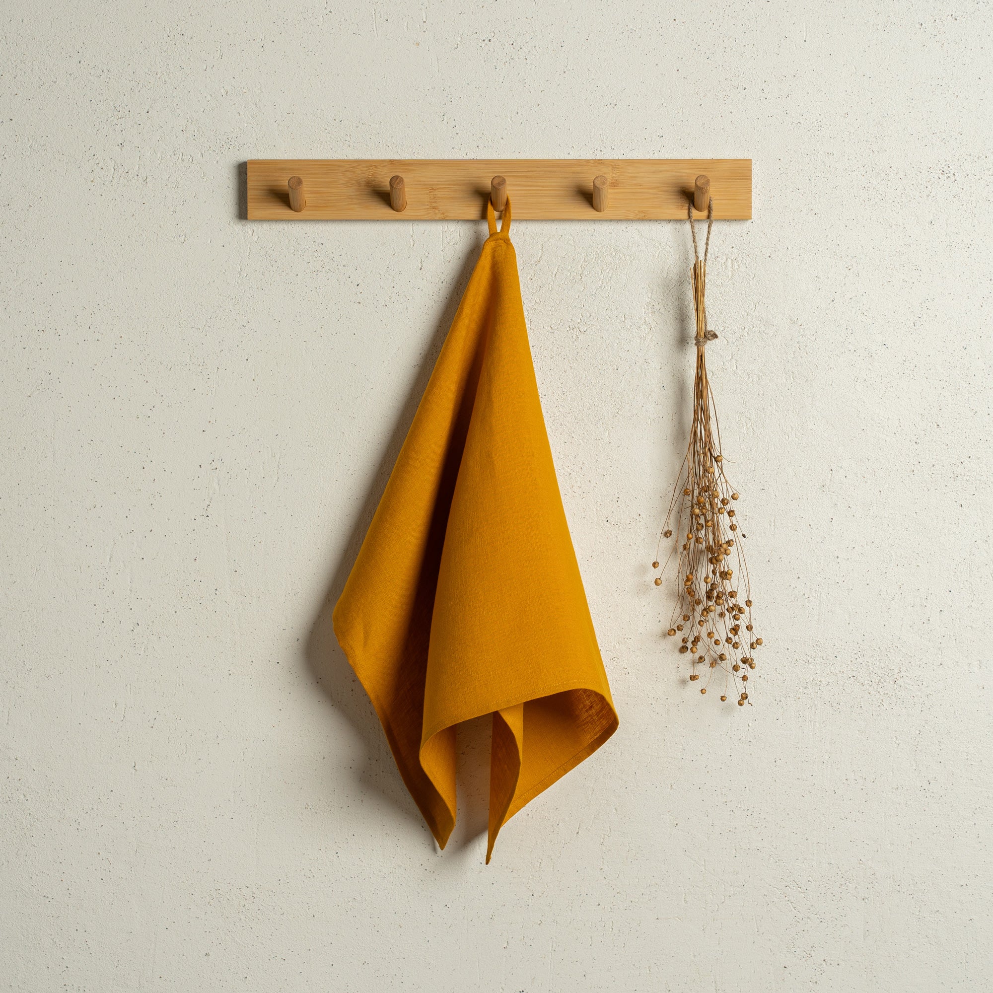 The menique linen kitchen dish towel in the color of spicy yellow hanging on a wooden rack on a wall.