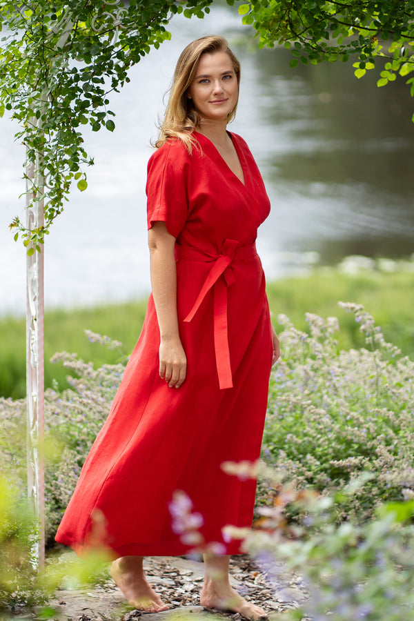 Woman in red wrap maxi dress standing in garden by lake, flowing feminine summer dress with waist tie