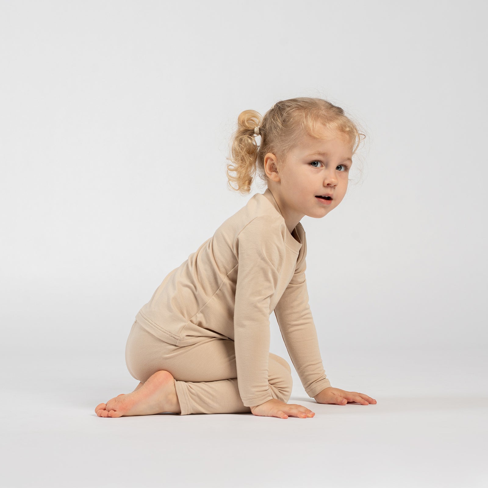 Side view of a person wearing beige bamboo long-sleeve top and matching leggings, standing on tiptoe against a light studio background.