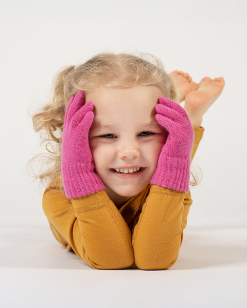 A young child with curly blonde hair and a bright smile wearing pink gloves on a white background