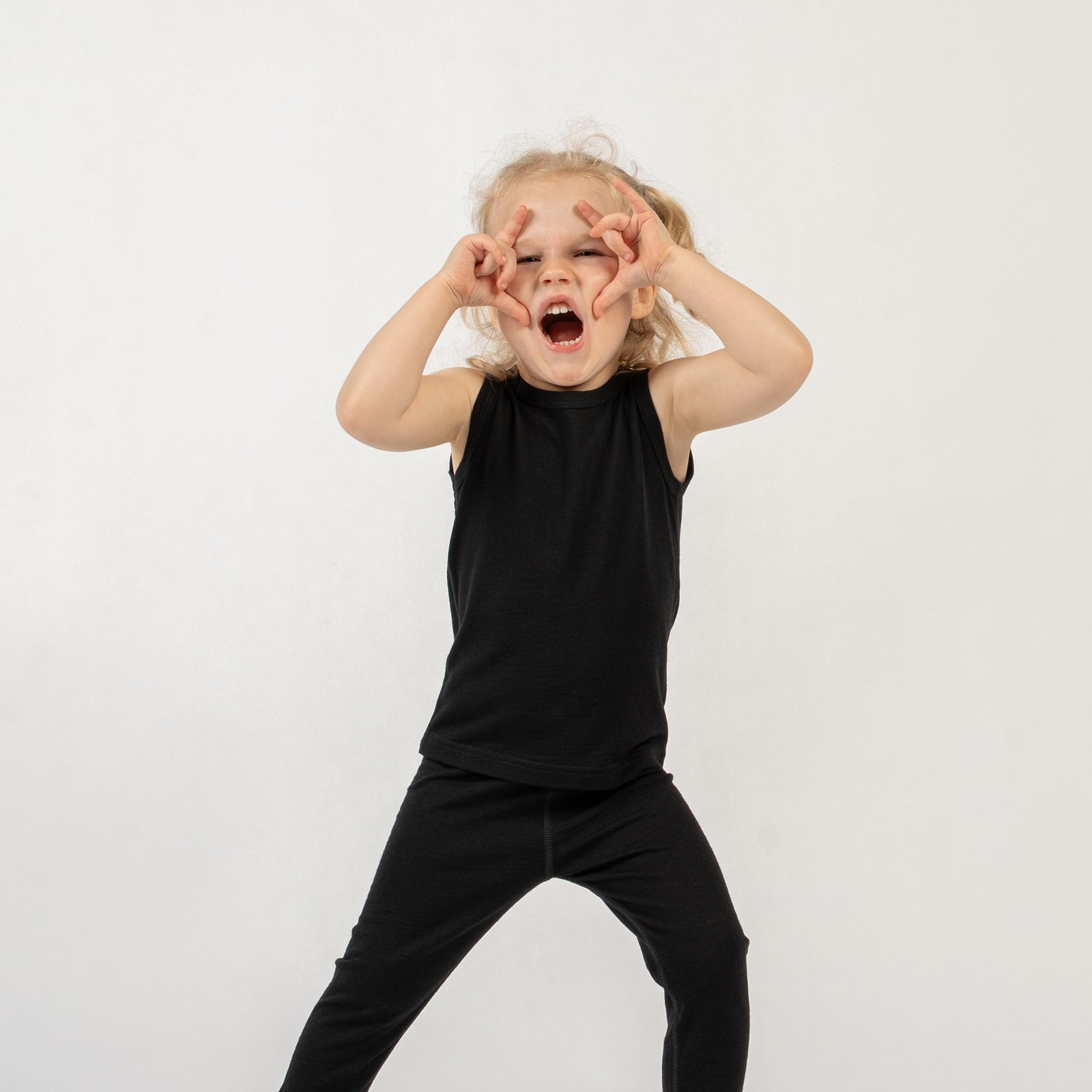Young child wearing a black menique sleeveless top made from merino wool and matching black pants on a white background