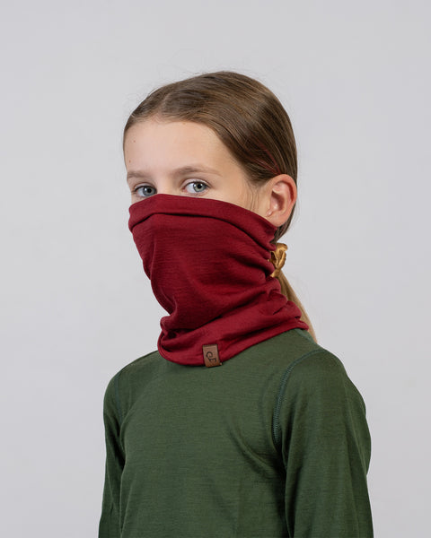 Girl in green top wearing a red Merino wool neck gaiter – versatile and comfortable kids’ winter wear.