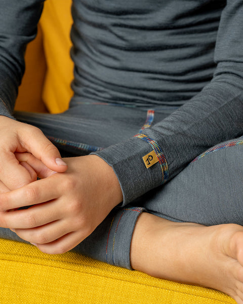 Close-up of a child’s hands and sleeve in a grey Merino wool base layer with multicolored seams, showing fabric texture and brand label.