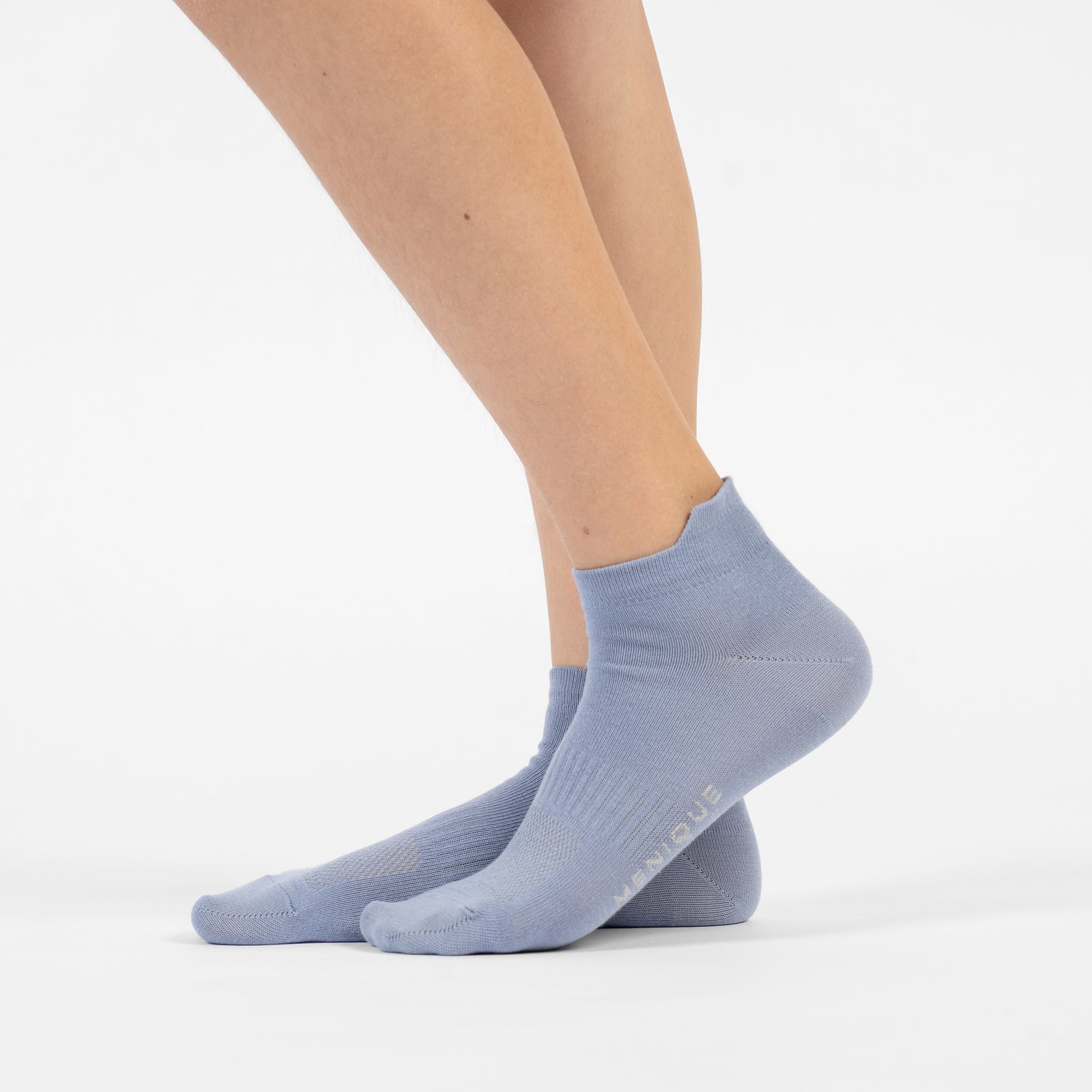 A person lying on their stomach with their lower legs raised, modeling a pair of dusty blue cotton ankle socks.