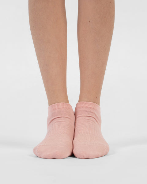 A front-facing view of a person's lower legs and feet standing flat on a white surface, wearing dusty pink cotton ankle socks.