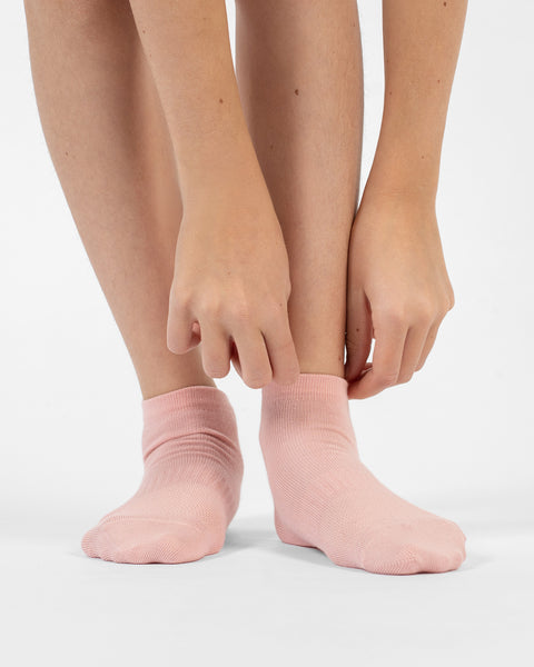 A front-facing view of a person's lower legs and feet, showing hands reaching down to adjust the cuff of a dusty pink cotton ankle sock.