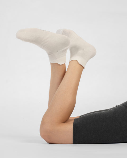 A person lying on their stomach with their lower legs raised, modeling a pair of natural white cotton ankle socks.