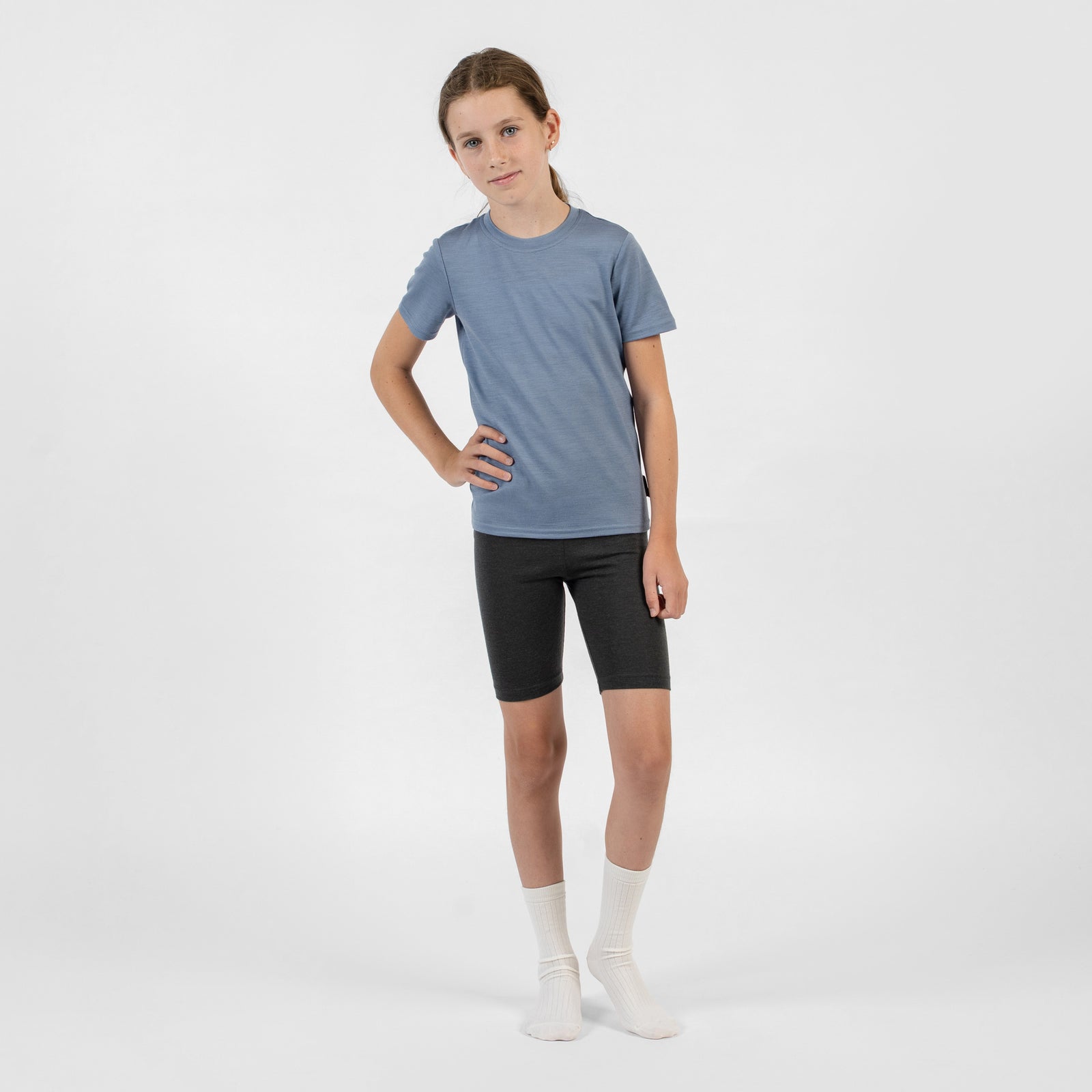 A front-facing close-up of a person's lower half wearing charcoal merino cycling shorts, with hands resting on their hips.
