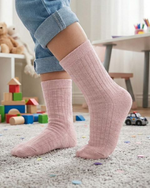 Child wearing pink merino wool socks standing in a playroom.