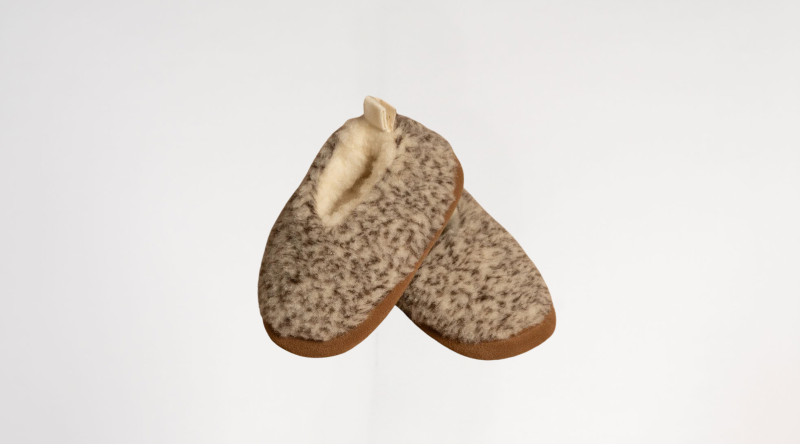 A close-up product shot of two fuzzy, grey-speckled wool slippers featuring brown edging and a plush cream-colored inner lining.