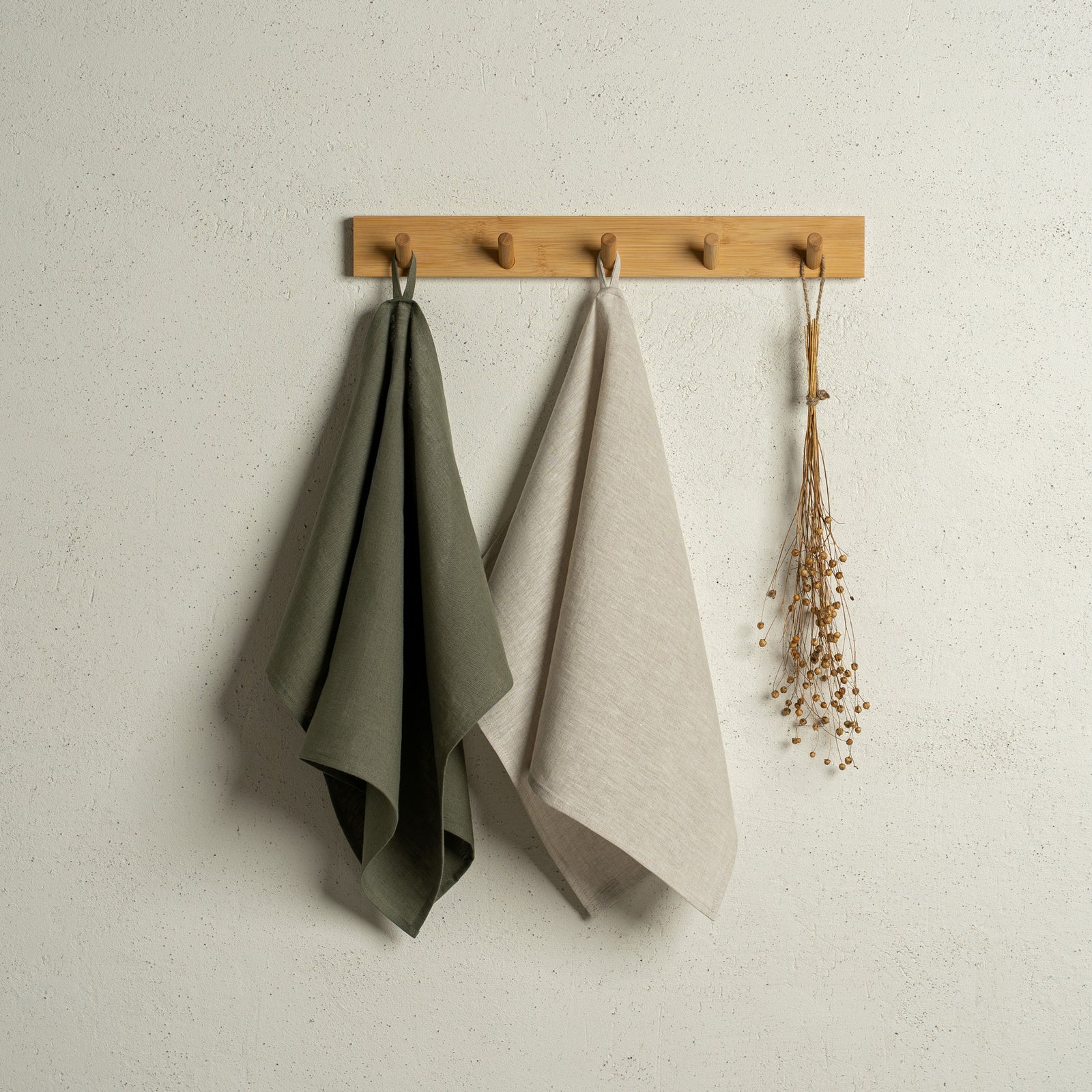 Two menique linen kitchen dish towels hanging on a wooden rack on a wall. The colors of the towels are stone green and green check. 