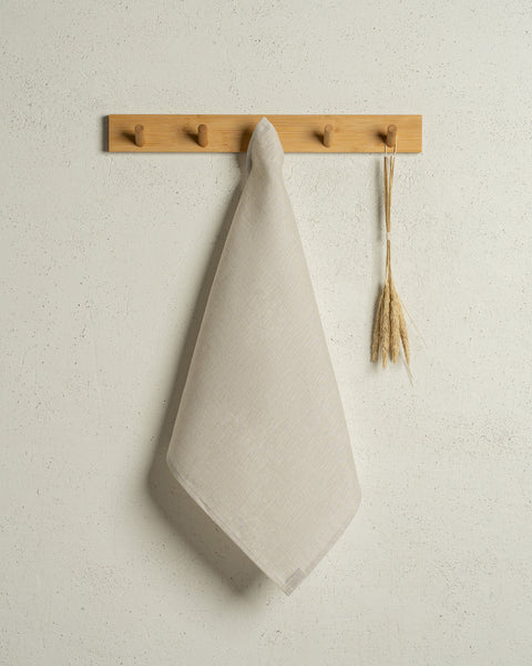 The menique square linen dish towel in color natural hanging on a wooden rack on a wall.