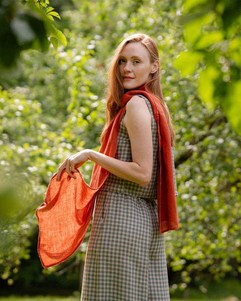 A woman wearing a checkered outfit and an orange scarf poses with their hands on the scarf.


