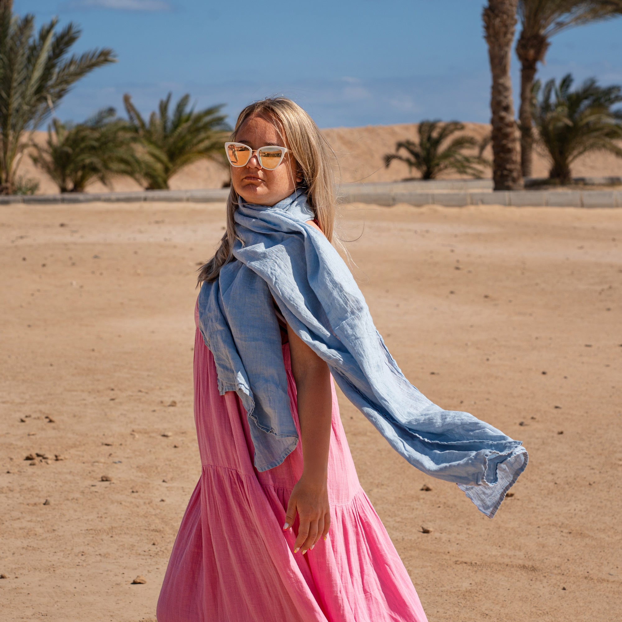 Women wearing Linen Scarf in Cloudy Blue color while in the background is seen palm trees