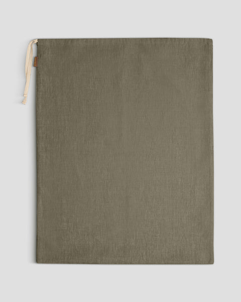 A large stone green linen drawstring bag lies flat against a light gray background, with its light-colored drawstrings gathered at the top left.