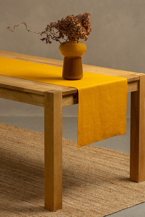 The menique spicy yellow color linen table runner on top of a wooden table. There is a vase on top of the runner.