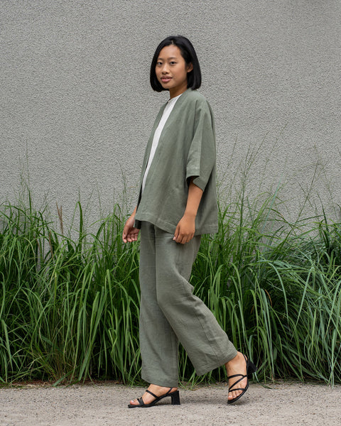 Woman with short dark hair wearing a stone green linen jacket and stone green menique pants.