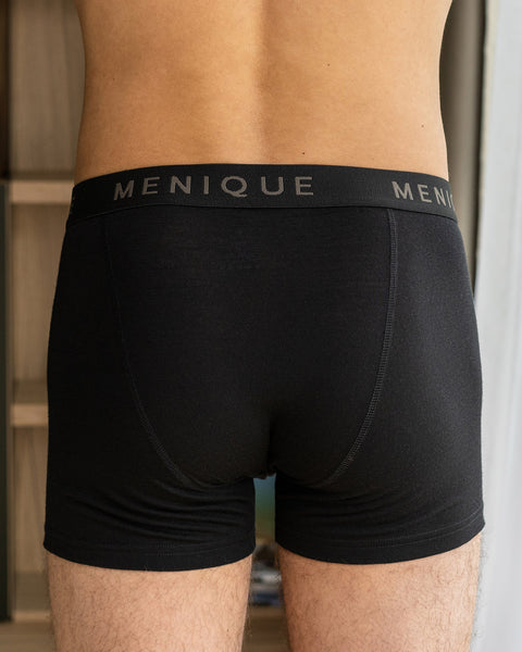 A man wearing short boxer briefs made from merino wool fabric, in color black. The back of the boxer shorts is visible in the photograph.